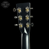 Close-up of the headstock of a black electric guitar, showing six tuning pegs with gold and silver accents against a solid black background. A Tone Shop watermark is visible in the top left corner.