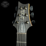 Close-up of a custom electric guitar headstock with six dark metal tuning pegs, a white script signature, and a dark gray pickguard that reads 'Custom'.