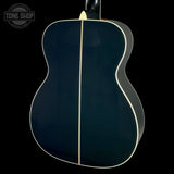 The back of an acoustic guitar with a glossy dark navy blue finish and a single light-colored center stripe, shown against a solid black background.