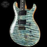 A double-cutaway electric guitar with a light blue and gold flamed maple top, black hardware, and a black pickguard, shown against a solid black background with a Tone Shop watermark in the top-left corner.