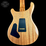 The back of an electric guitar with a natural wood finish and black pickguards, shown against a solid black background with a Tone Shop watermark in the top left corner.
