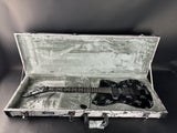 Black electric guitar in a gray case on a dark background