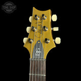 Close-up of a gold metallic electric guitar headstock with cream tuning pegs and a dark fretboard, shown against a black background. A Tone Shop watermark is visible in the top-left corner.