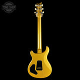 A gold electric guitar shown from the back against a solid black background, featuring a glossy metallic gold finish, black pickguard, and white tuning pegs.