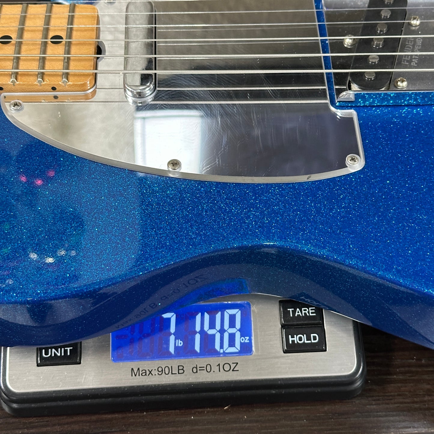 Blue electric guitar on a digital scale displaying weight.