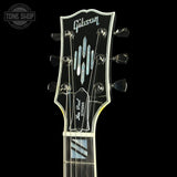 Close-up of a Gibson Lita Grand electric guitar headstock and upper neck against a solid black background, featuring a black headstock with silver hardware and blue/white inlays.