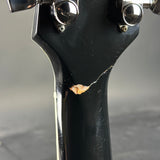 Close-up of the headstock of a black electric guitar, showing a cracked finish and a worn, orange-brown exposed wood patch near the lower part of the neck.