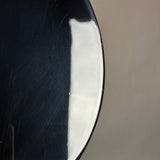 Close-up of a glossy black curved surface with a bright white reflection against a plain taupe-gray background.