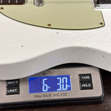 Close-up of a white electric guitar body resting on a digital scale displaying 6 lbs 30 oz.