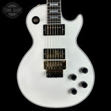 White electric guitar with a black pickguard on a black background, featuring the Tone Shop logo.