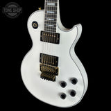 White electric guitar with a black pickguard on a black background, featuring the Tone Shop logo.