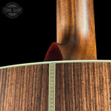 Close-up detail of an acoustic guitar body and neck, showing rich wood grain, a decorative inlay line, and a dark reddish-brown headstock end against a black background. A Tone Shop watermark is visible in the top left.