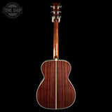The back of an acoustic guitar with a rich reddish-brown wood grain finish, shown against a solid black background. A circular 'TONE SHOP' watermark is visible in the top-left corner.