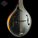 A close-up studio shot of a mandolin against a solid black background, showing its glossy black body, f-holes, six strings, and a natural wood edge. A 'TONE SHOP' watermark is visible in the top-left corner.