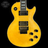 Yellow electric guitar with a black pickguard on a black background, featuring the Tone Shop logo.