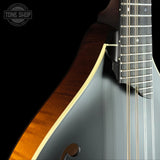 Close-up of a mandolin showing the glossy dark gray body, the warm brown wood side edge, the cream binding, and part of the dark fretboard with metal frets against a black background. A 'TONE SHOP' watermark is visible in the top-left corner.