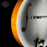 Close-up of a double-cutaway electric guitar showing the glossy orange-brown wood back, matte gray body, f-hole, strings, and part of the headstock against a black background. A Tone Shop watermark is visible in the top-left corner.