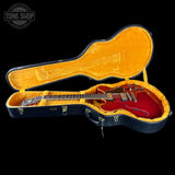 Red electric guitar in an open black and yellow case with 'Tone Shop' logo.