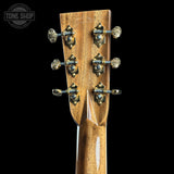 Close-up of the headstock of a wooden stringed instrument, showing the back side with six ornate gold-toned tuning pegs on a black background. A Tone Shop watermark is visible in the top left corner.