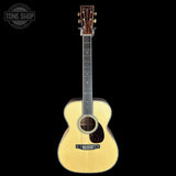 A natural wood acoustic guitar with a dark headstock, shown vertically against a solid black background. A circular 'TONE SHOP' watermark is visible in the top-left corner.