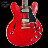 Red electric guitar with a black pickguard on a black background, featuring the Tone Shop logo.