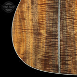 Close-up of a guitar body showing a rich, figured wood grain pattern in warm brown and golden tones, with a decorative white inlay running vertically. A Tone Shop watermark is visible in the top-left corner.