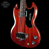 Red electric bass guitar on a black background with 'Tone Shop' logo.
