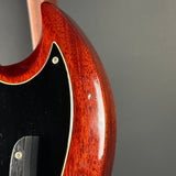Close-up of a guitar's wooden neck and black pickguard on a gray background