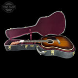 An acoustic guitar with a sunburst finish displayed inside an open black hard case with a burgundy interior, set against a solid black background. A 'TONE SHOP' watermark is visible in the top-left corner.