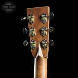 Close-up of the headstock of a guitar, showing six tuning pegs and a brown wood grain finish, set against a solid black background.