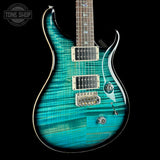 A turquoise blue electric guitar with a flamed maple top and silver hardware, shown against a solid black background with a Tone Shop watermark in the upper left corner.