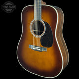 A classic acoustic guitar with a natural sunburst finish, featuring a dark brown center, fading to a warm amber-brown edge, with a black pickguard and white binding, shown against a solid black background.