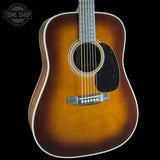 A classic acoustic guitar with a natural sunburst finish, featuring a dark black pickguard and a silver-toned bridge, shown against a solid black background with a Tone Shop watermark in the top left corner.