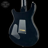 The rear view of a black electric guitar body with a satin black finish, featuring a silver pickguard, gold bridge plate, and a black neck, shown against a black background with a Tone Shop watermark in the top left corner.