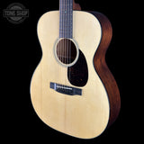 An acoustic guitar with a natural light wood top and a dark brown wooden body, shown against a solid black background. A Tone Shop watermark is visible in the upper left corner.