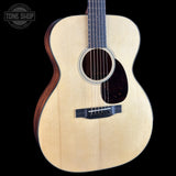 An acoustic guitar with a natural wood top and dark brown sides, shown against a solid black background with a Tone Shop logo in the upper left corner.