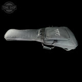 A dark gray acoustic guitar or ukulele gig bag with a front zippered pocket featuring a white script logo, shown against a solid black background. A Tone Shop watermark is visible in the top-left corner.