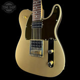 A gold-finished electric guitar with black pickguard and hardware, shown against a solid black background. A Tone Shop watermark is visible in the top-left corner.