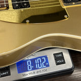 Close-up of a gold electric guitar body resting on a digital scale displaying 8 lbs 102 oz, with the scale showing brand text 'GEMBA'.