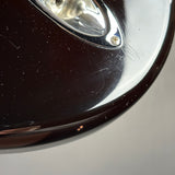 Extreme close-up of a glossy dark brown or black curved surface with a silver metal accent and visible scratches and dust on the finish.