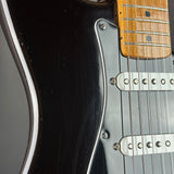 Close-up of a black electric guitar body with a maple neck, silver hardware, and white pickguard.