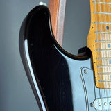 Close-up of a black electric guitar body with a maple neck and silver hardware against a dark gray background.