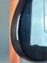 Close-up of the glossy black body edge of an electric guitar, showing visible scratches and wear on the finish.