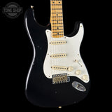 Black electric guitar with a white pickguard on a black background, featuring 'Tone Shop' branding.