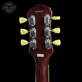 Close-up of the headstock of a six-string acoustic guitar, showing six yellow tuning pegs, chrome tuning machines, and a dark reddish-brown glossy finish against a black background.