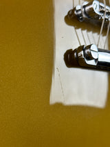 Close-up of a metallic gold guitar body with part of the bridge and strings visible, photographed against a matching gold surface.