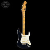 Electric guitar with a black body and white pickguard on a black background, featuring the Tone Shop logo.
