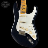 Black electric guitar with a white pickguard on a black background, featuring the Tone Shop logo.
