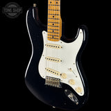 Black electric guitar with a white pickguard on a black background, featuring 'Tone Shop' branding.