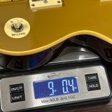 A close-up of a gold electric guitar body resting on a digital scale displaying 9.04 oz, with the guitar's white footswitch and part of the headstock visible.